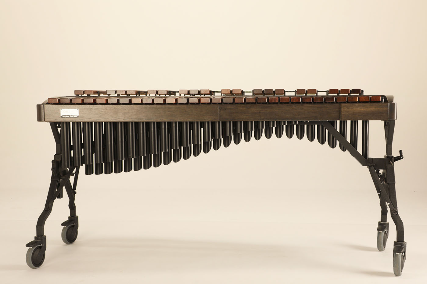 A professional dark wood marimba with multiple rows of brown and reddish wooden bars, black resonators in varying lengths, and a black stand with wheels on a light background.