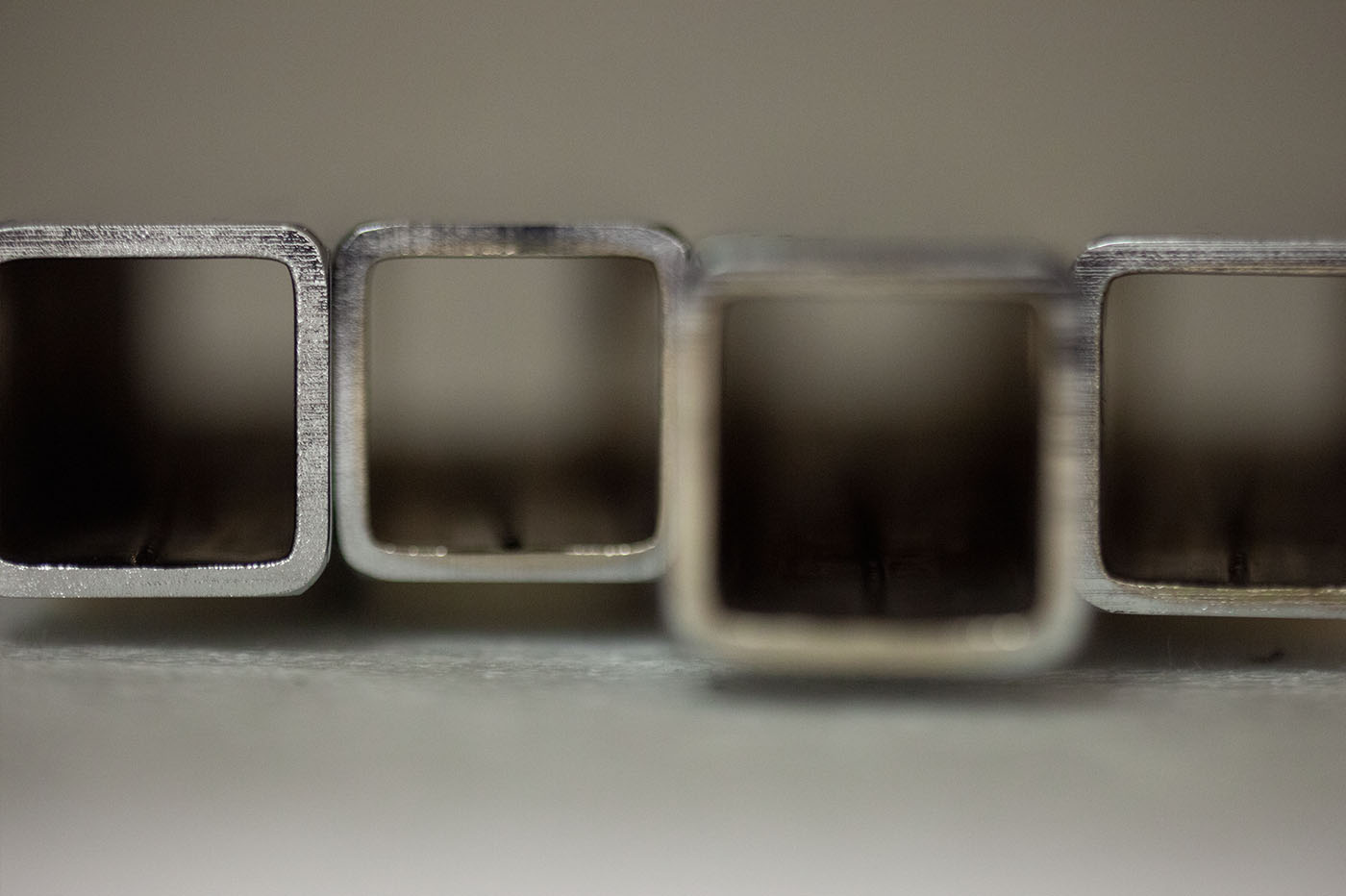 Close-up of four rectangular metal tubes, likely aluminum or steel, showcasing their internal hollow structure and metallic surfaces.