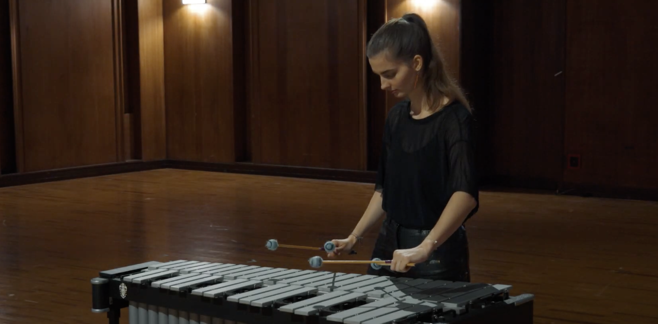 Young woman performing on a Musser M55 vibraphone in a music room with dark wood paneling.
