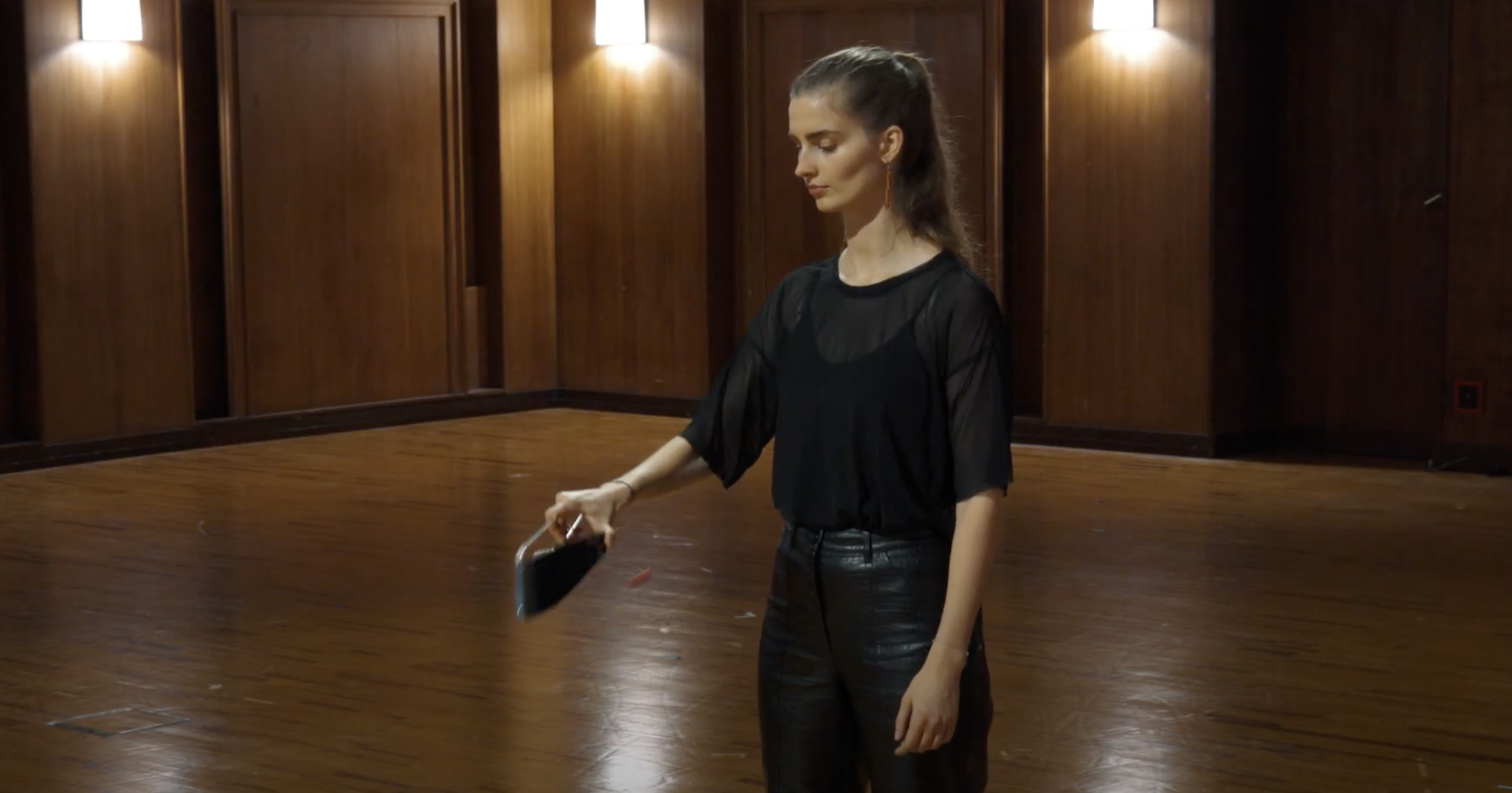Woman demonstrating large flexatone musical instrument in a wooden room.