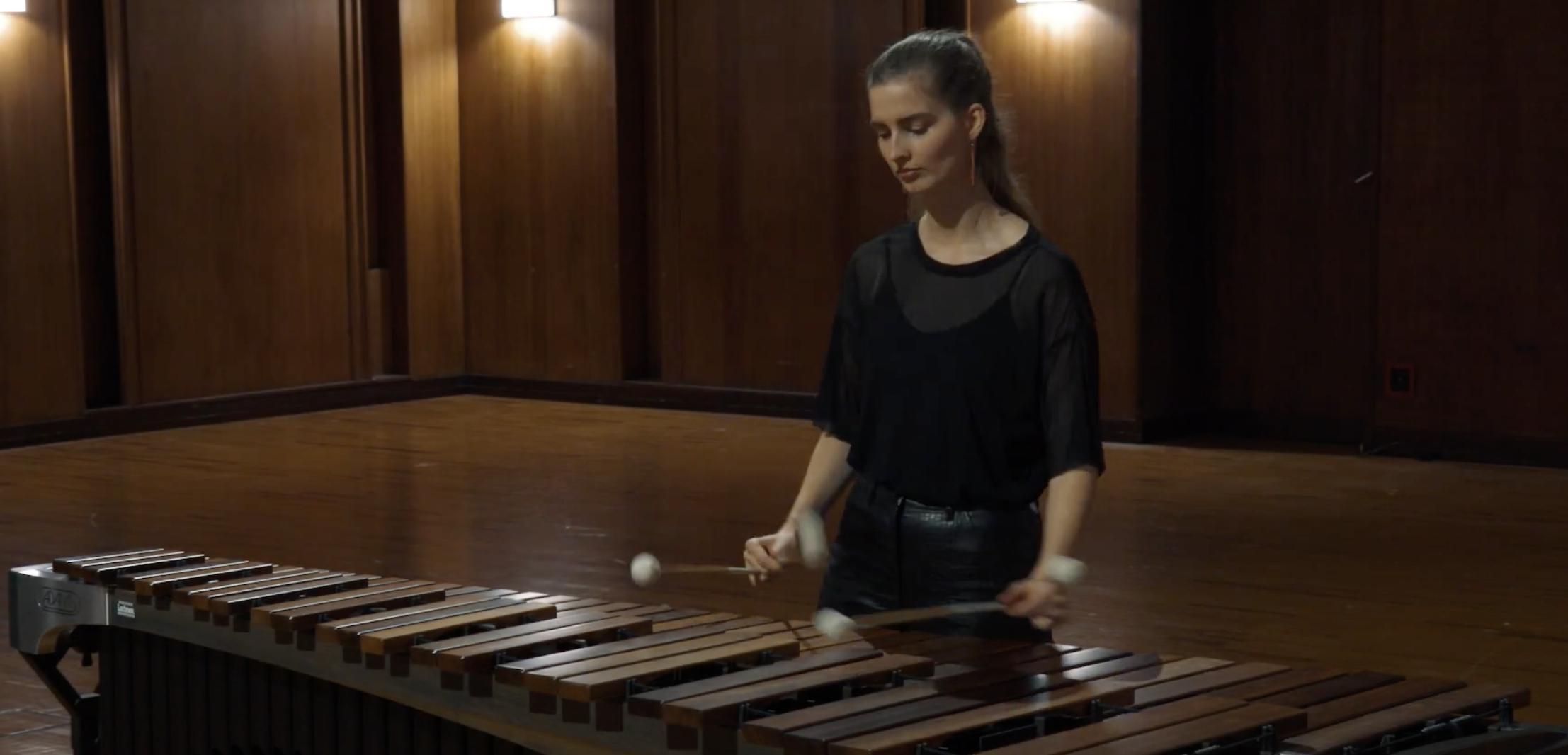 Full body shot of a woman playing the marimba, focused on her instrument in a performance hall.