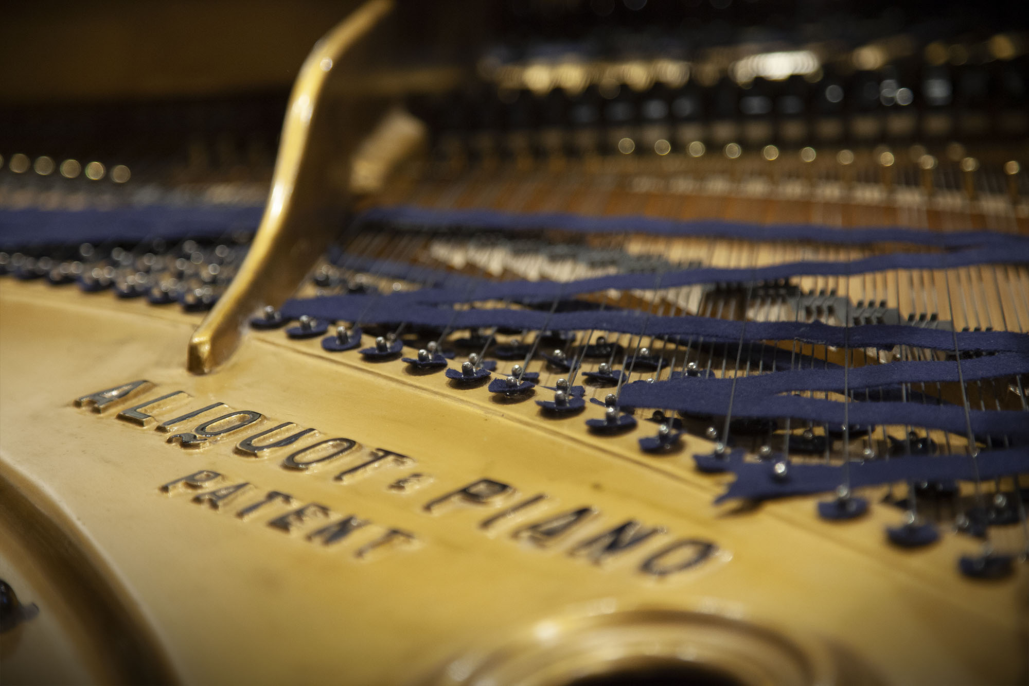 Close-up of a grand piano's interior, showing strings, dampers, and the inscription Aliquot Piano Patent on the golden soundboard, highlighting its intricate mechanics.