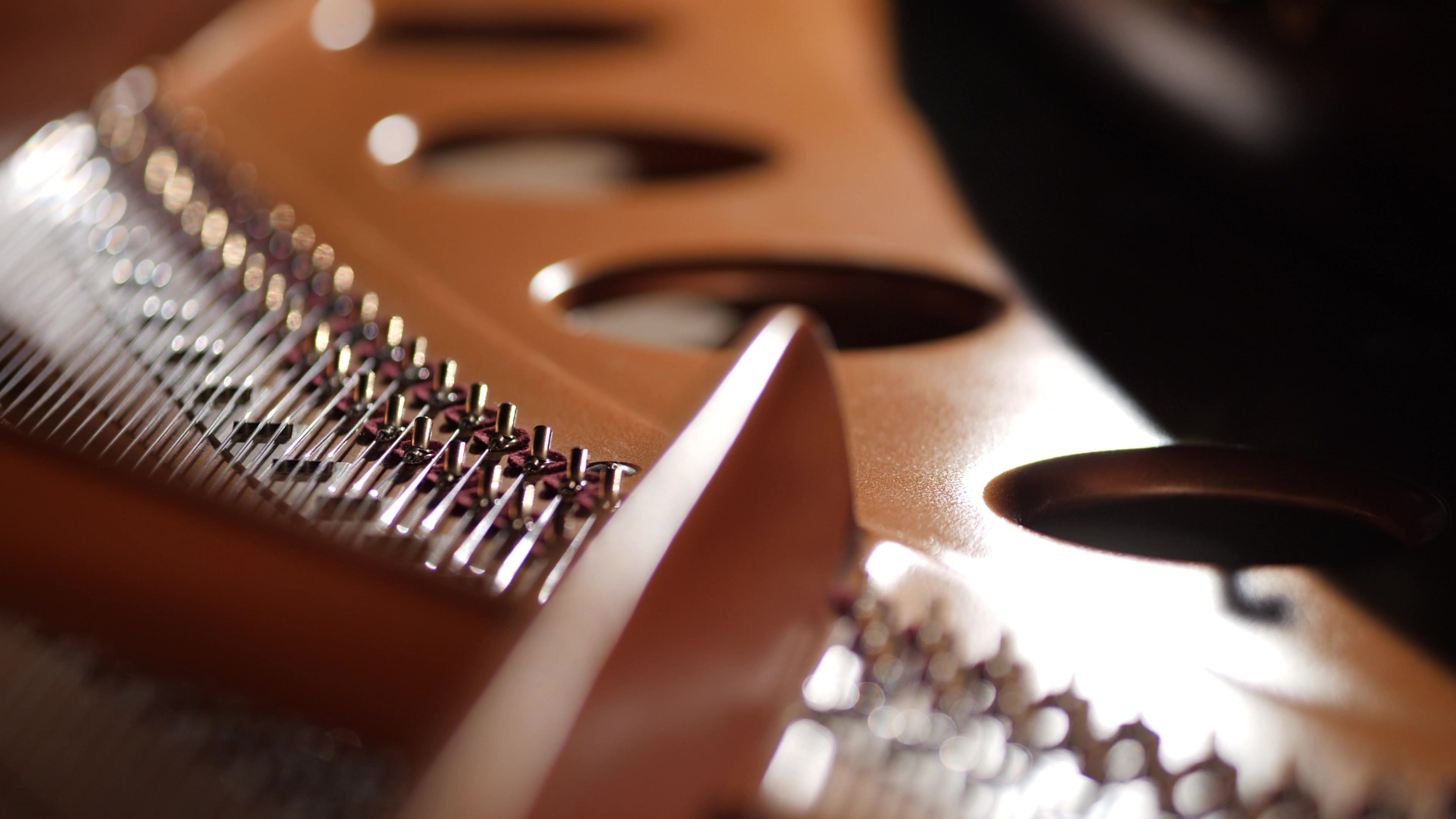 Close-up of a grand piano's interior, showing strings, tuning pins, and soundboard in warm light.