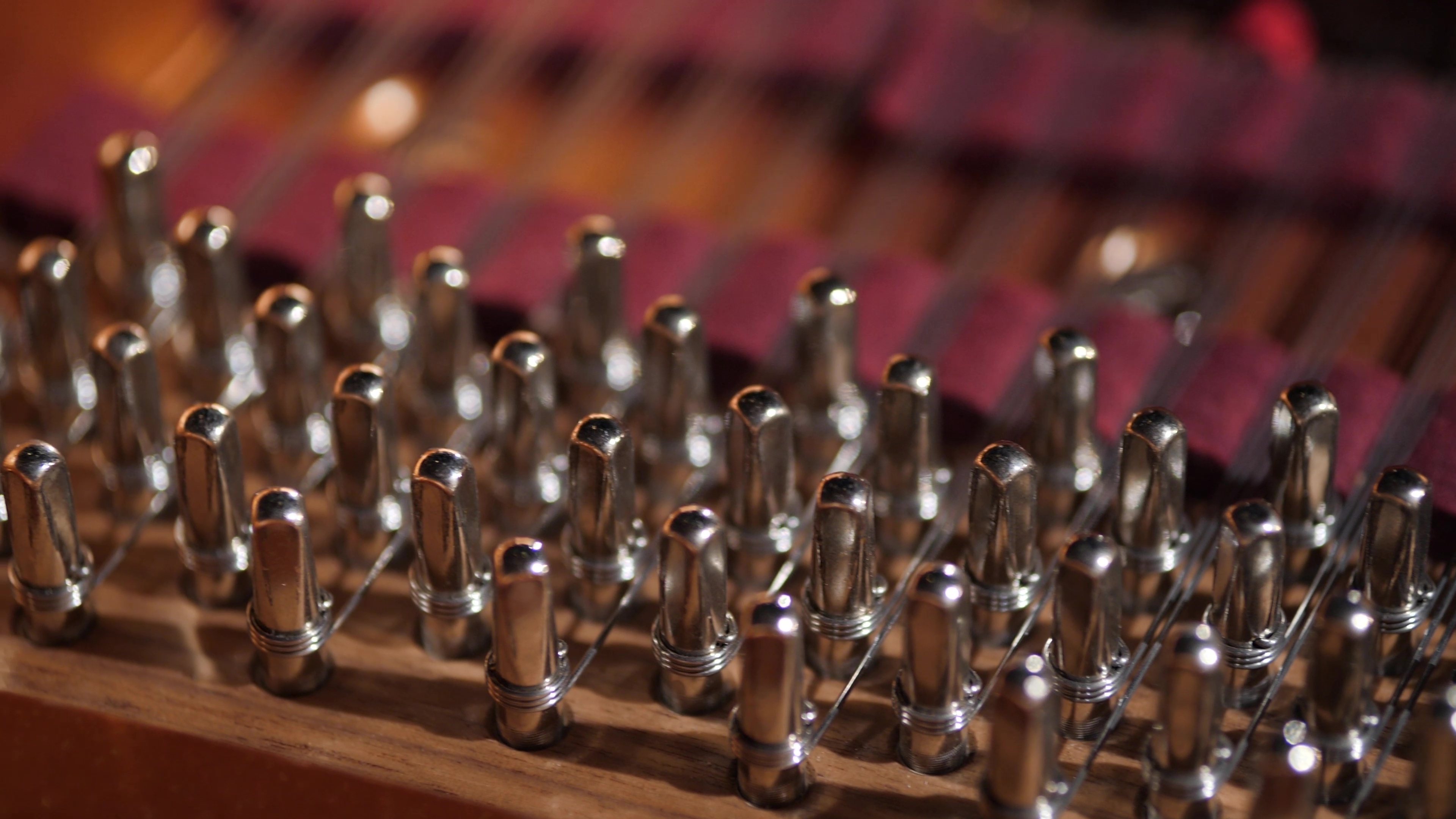 Close-up of a hammered dulcimer's tuning pins and strings, showing the intricate detail of the musical instrument's hardware and strings against a blurred background.