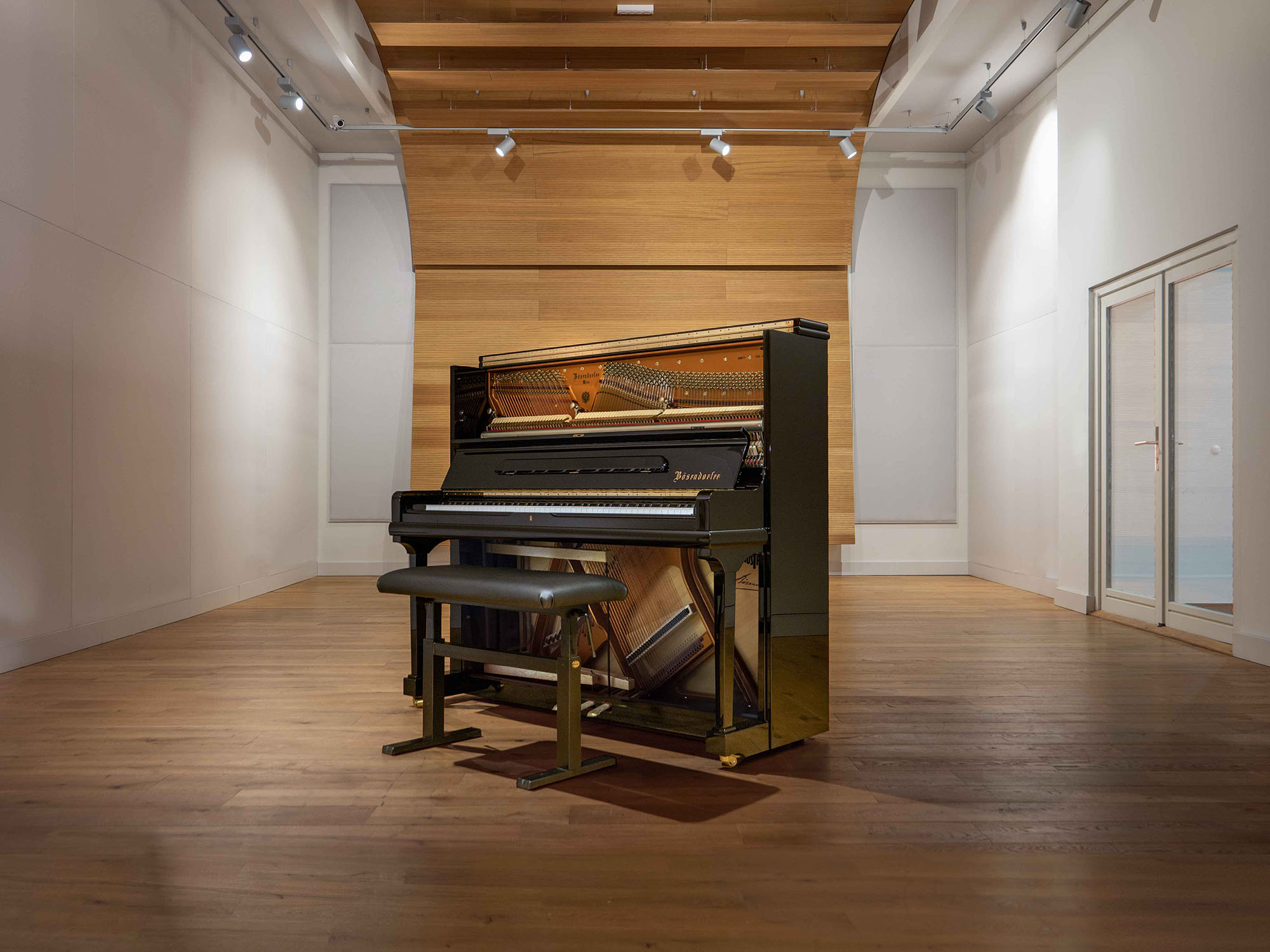Black upright piano with open top and accompanying bench in a well-lit modern room with wooden floors and accent walls