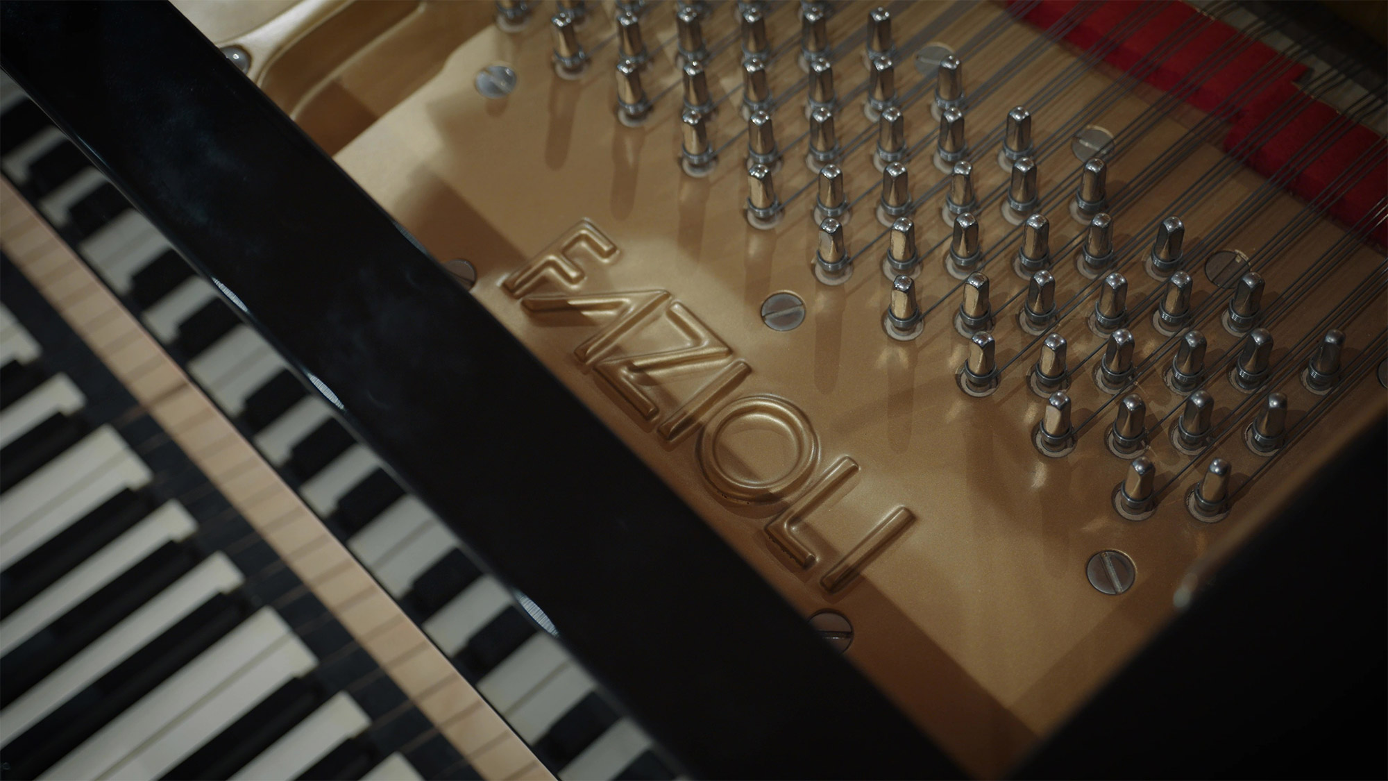 Fazioli grand piano interior showing the golden soundboard, tuning pins, strings, and keys.