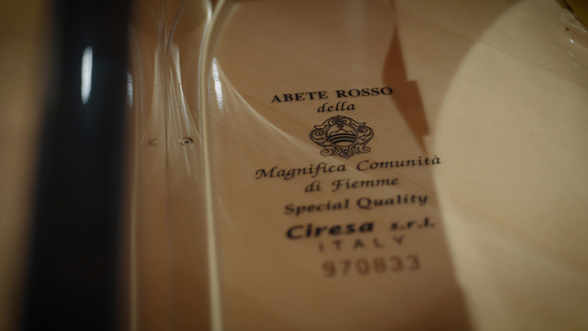 Close-up of a light-colored wooden instrument interior, showcasing a dark stamp with text Abete Rosso Della, Magnifica Comunità di Fiemme, Special Quality, Ciresa S.R.L. Italy, and a serial number 970833, along with a decorative crest.