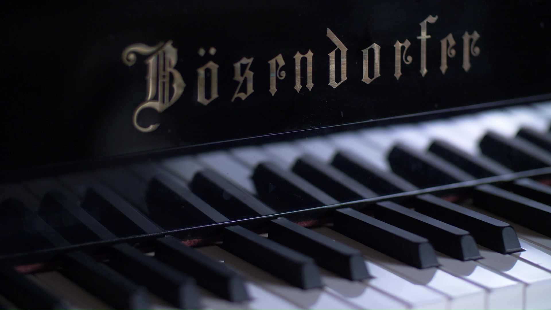 Close-up view of a Bösendorfer piano, centered on the brand name on the instrument's fallboard, with the black and white keys of the keyboard visible in soft focus below.