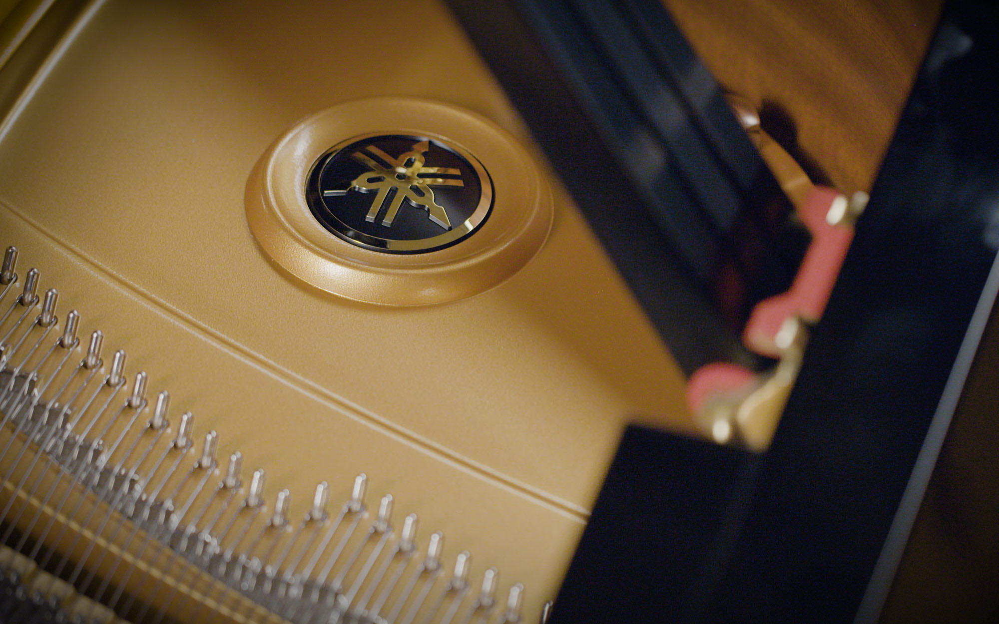 Close-up of the Yamaha logo emblem on a gold soundboard inside a grand piano, showing internal mechanisms like piano strings and tuning pins.