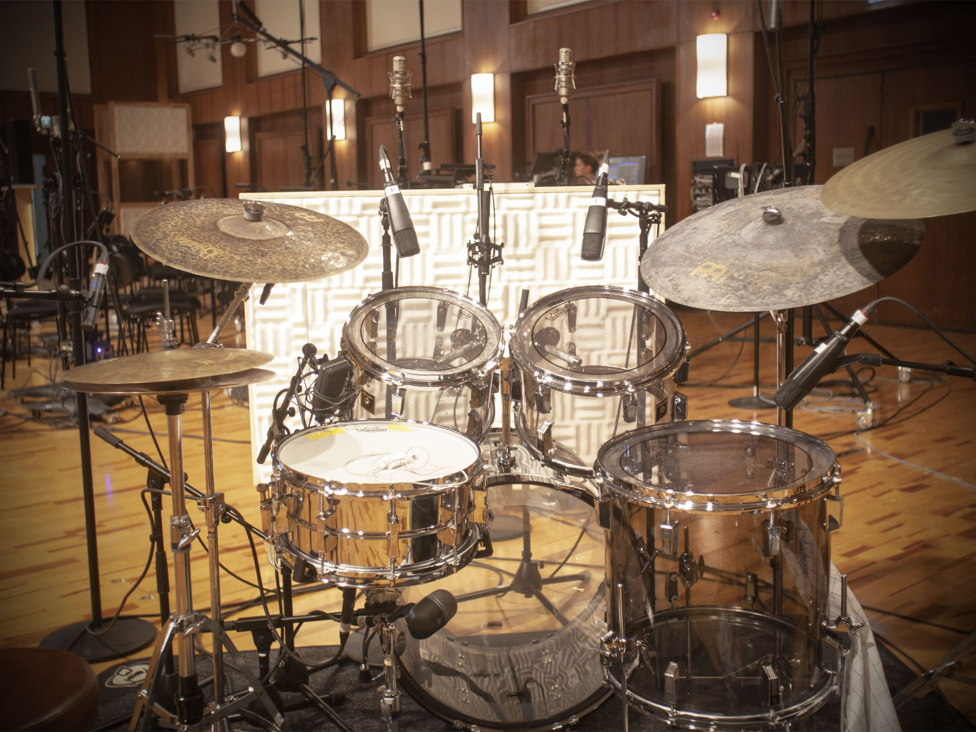 A complete drum set in a recording studio, featuring cymbals, snare drum, bass drum, and tom-toms, with multiple microphones positioned around the kit.