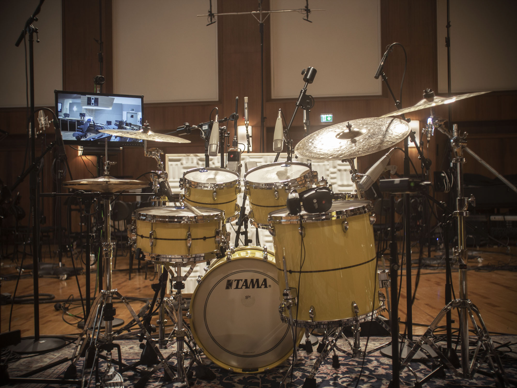 Full drum kit with yellow Tama drums and cymbals in a professional recording studio, surrounded by microphones and audio equipment