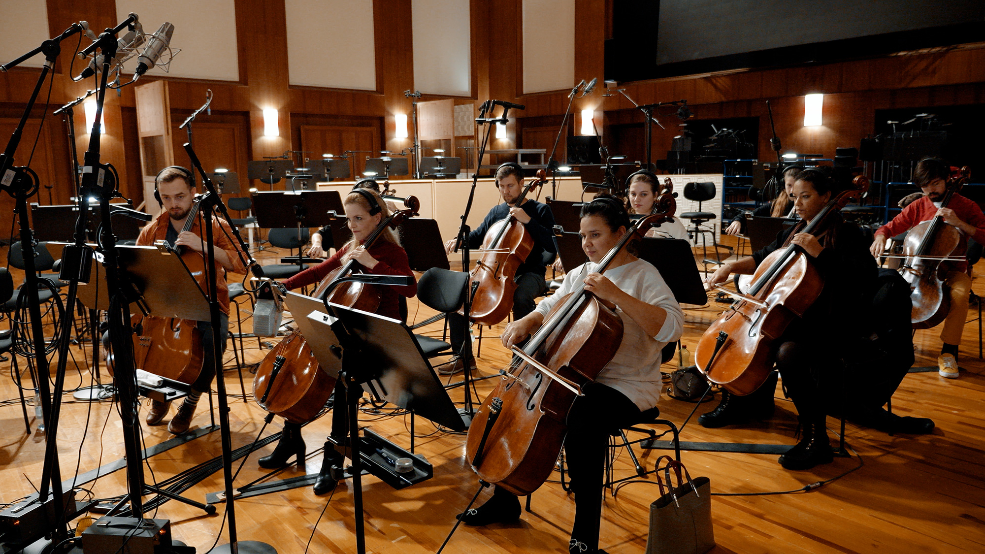 Cello ensemble recording music in a studio with professional microphones and stands.