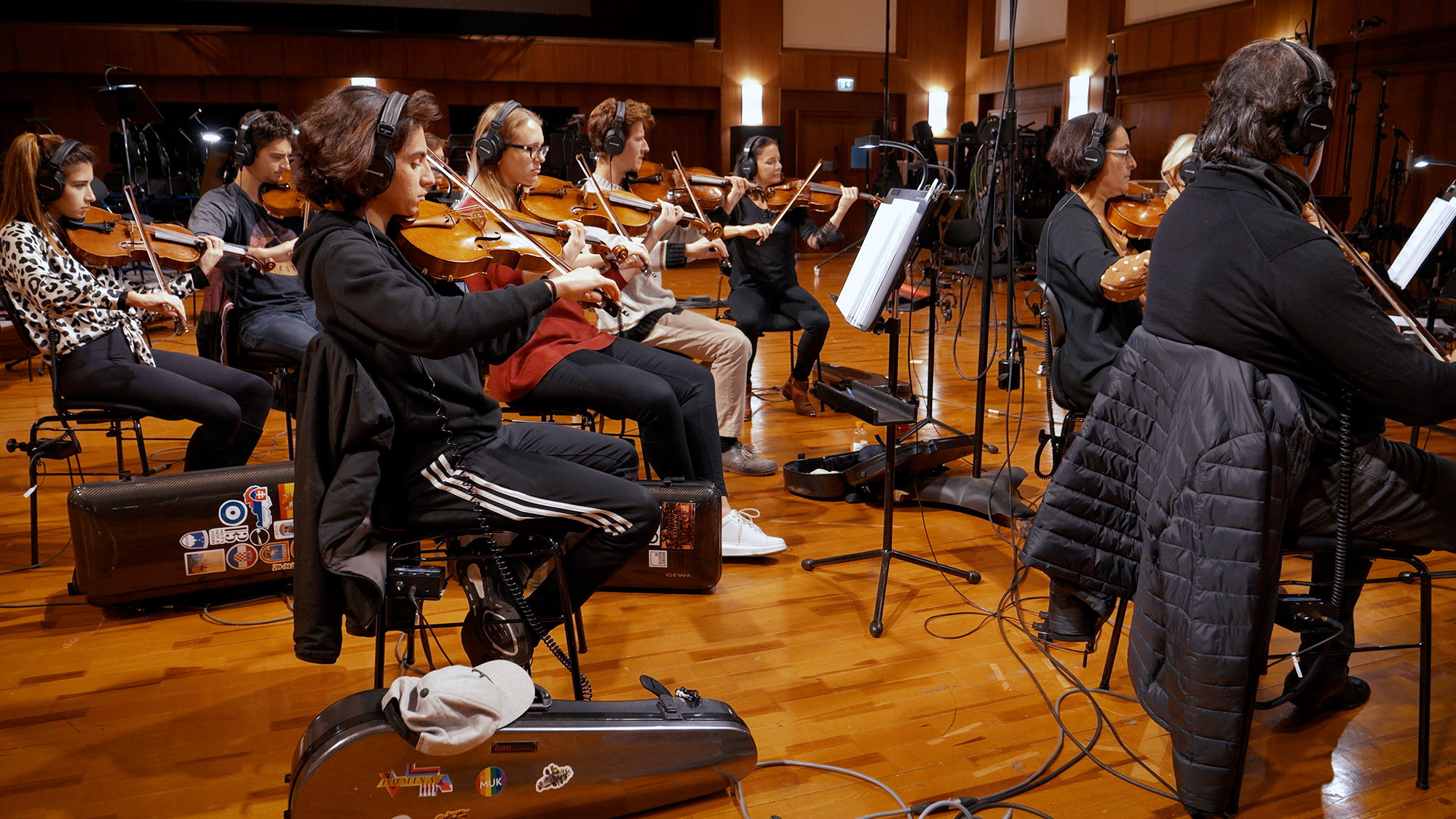 Musicians with headphones playing violins in a recording studio, highlighting a diverse orchestra during a professional music production session.