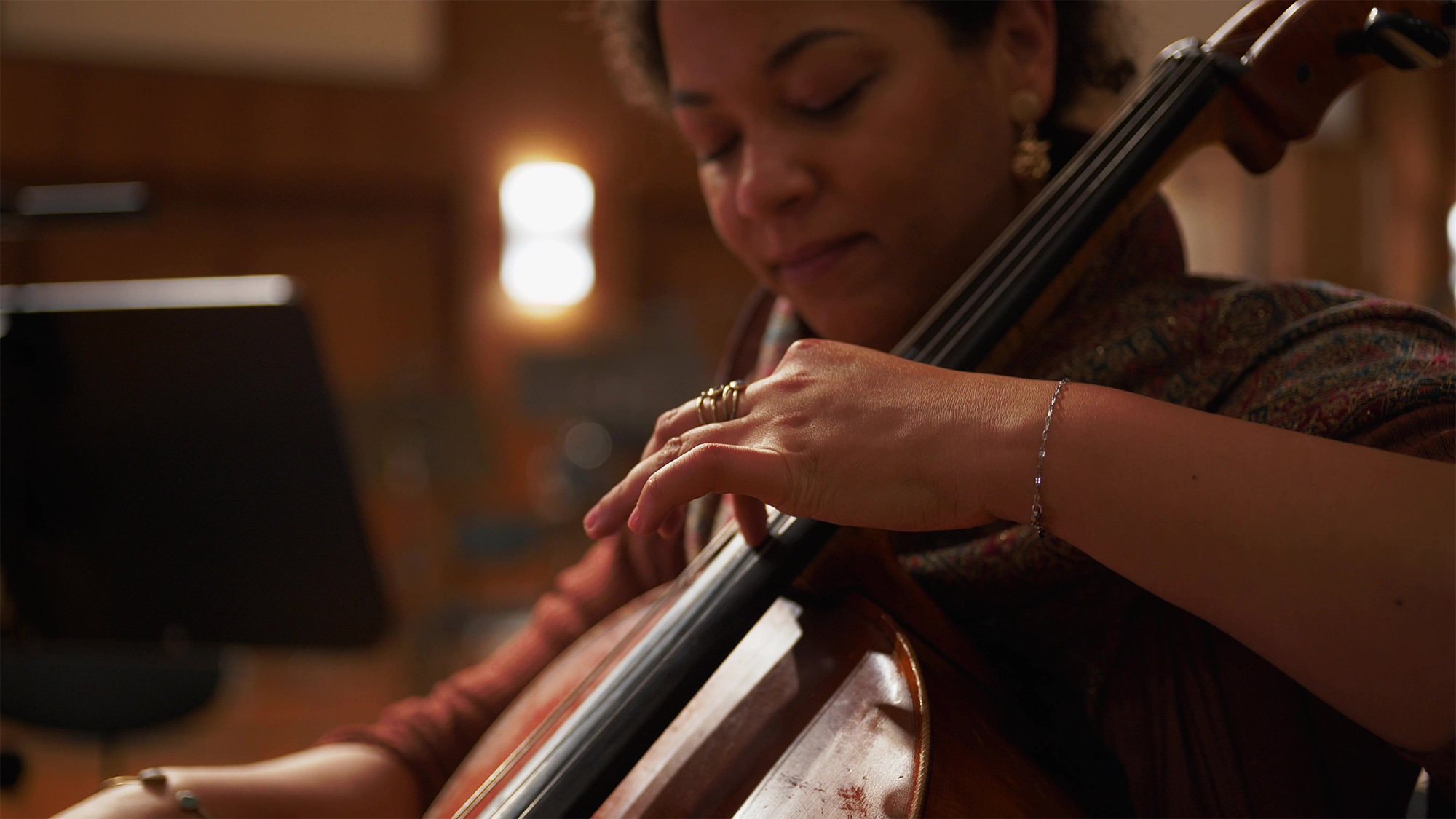 Close-up of a female cellist playing her instrument, showing her focused expression and hands on strings.