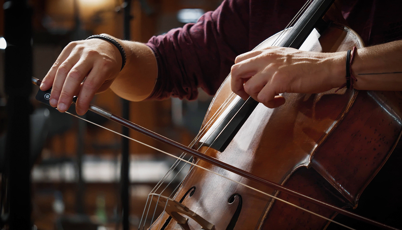 Close-up of a musician's hands playing a cello with a bow, showcasing the rich wood tones and strings of the instrument.