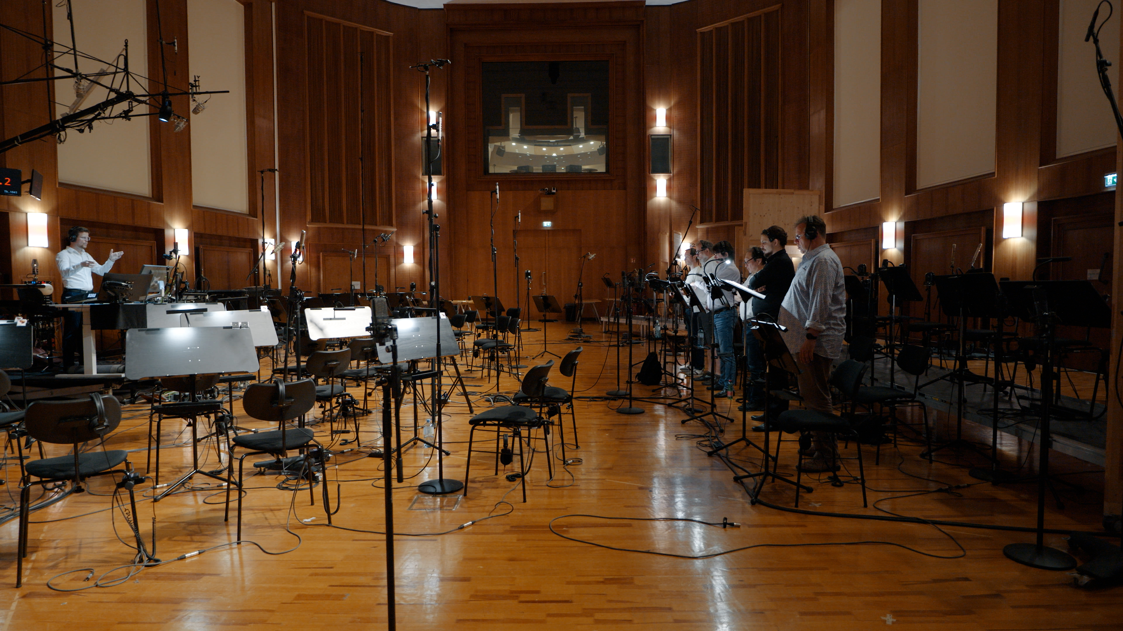 Recording studio session with a conductor, an orchestra, microphones, music stands, and chairs, ready for classical music recording.