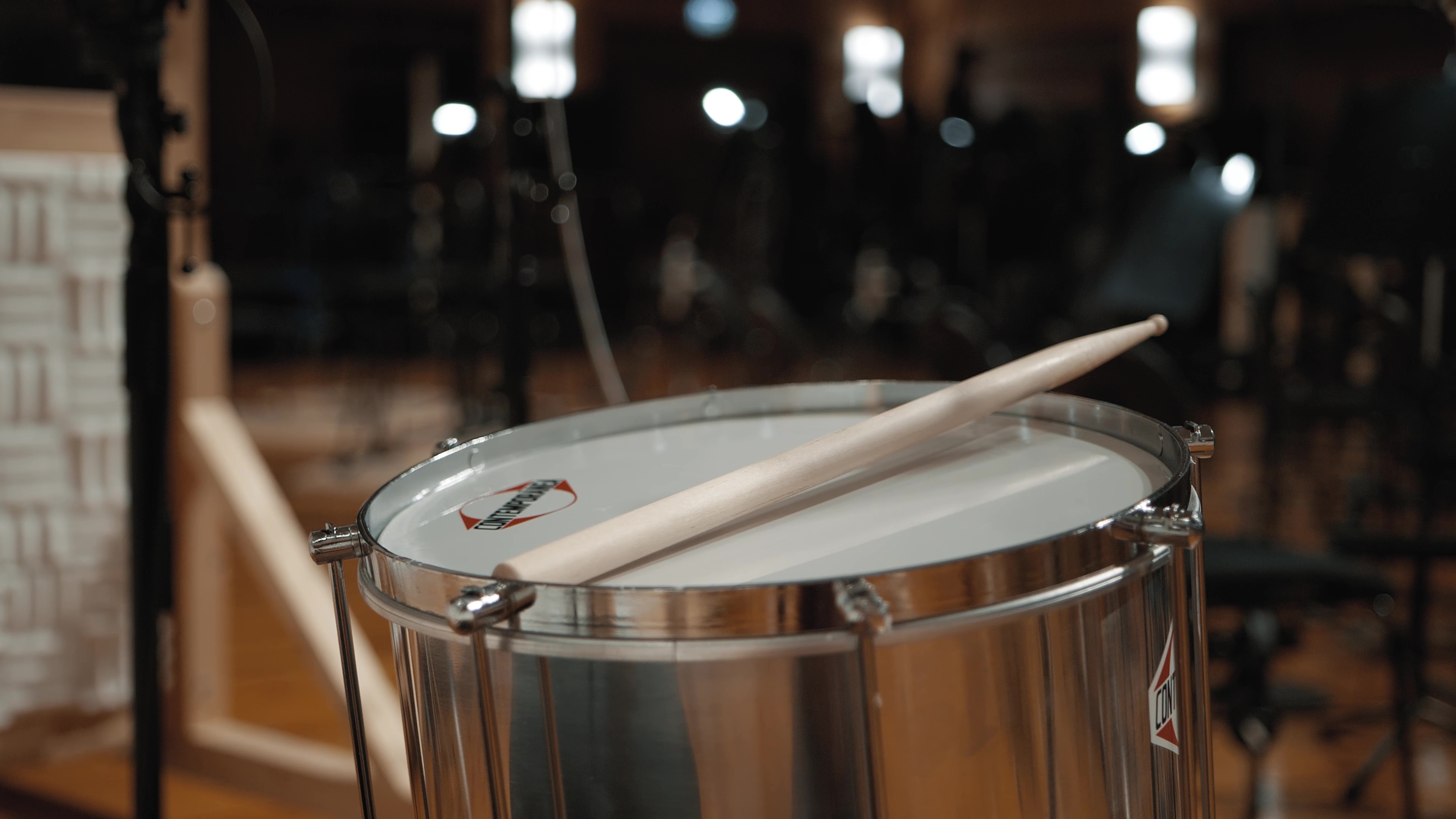 Wooden drumstick resting on a silver snare drum in a recording studio.