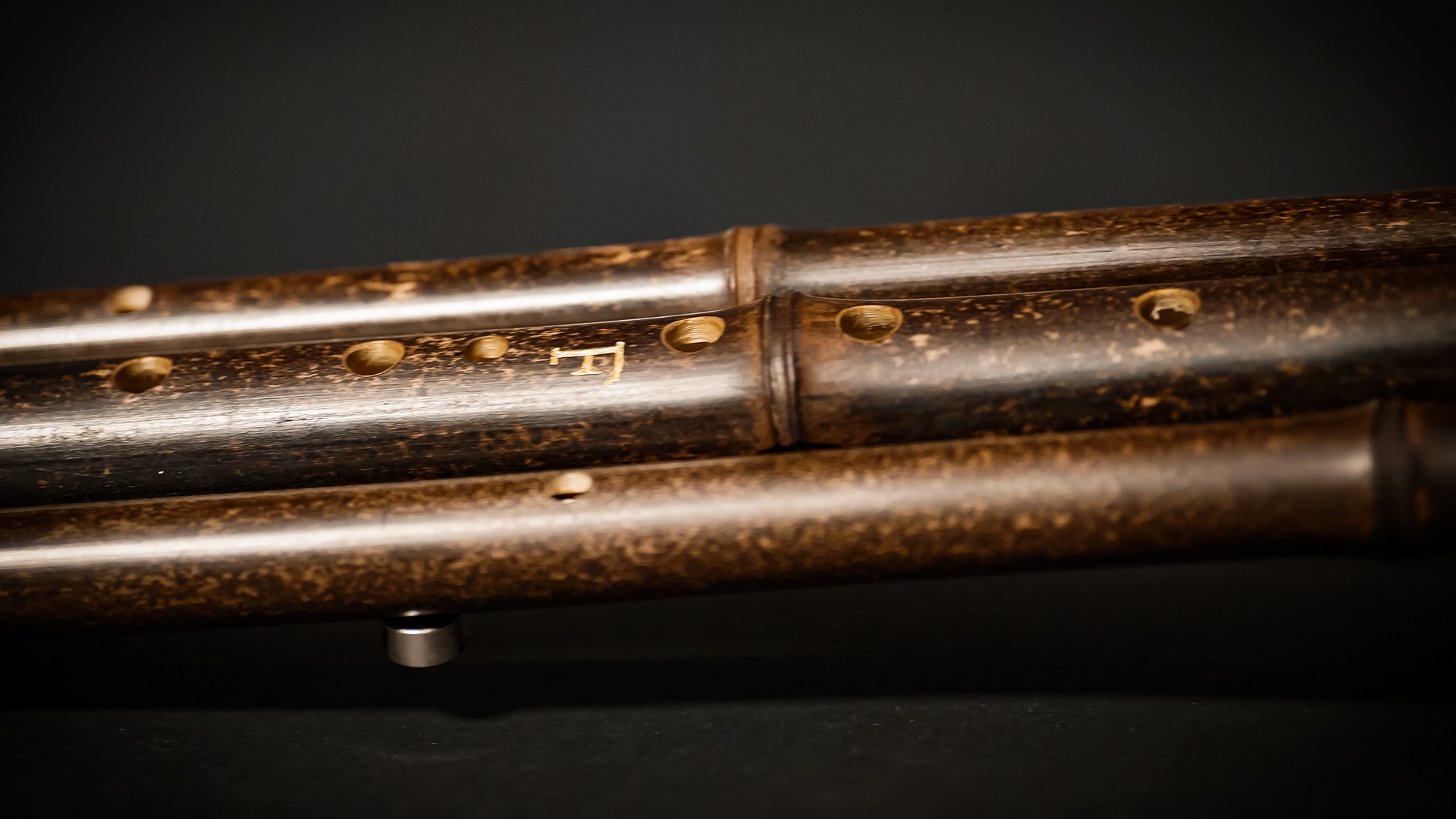 Close-up of a dark brown bamboo Japanese musical instrument, shakuhachi flute, showing its natural wood grain, finger holes, and the engraved F clef symbol.