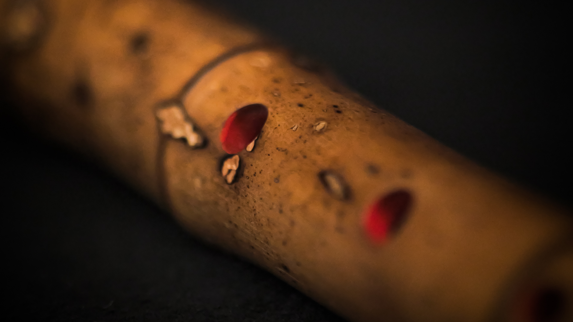 Close-up of a brown, speckled wooden flute with two vivid red depressions, likely finger holes, against a dark background.