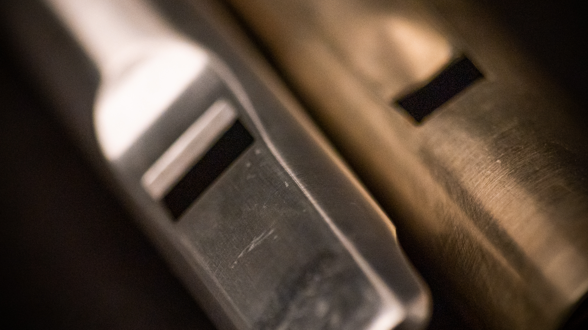Close-up of a silver and a brass pipe organ flue pipe showing the mouth opening, light reflections, and textured surfaces