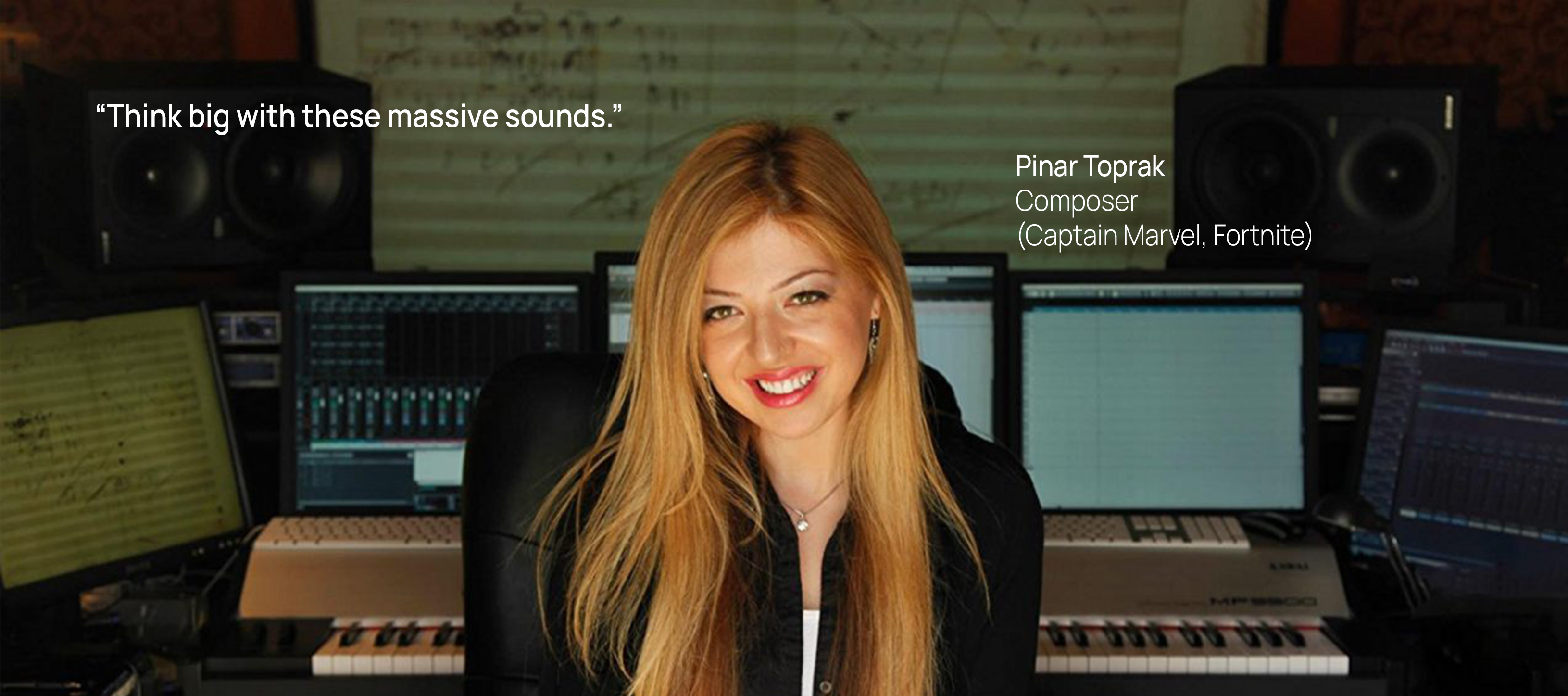 Pinar Toprak, composer for Captain Marvel and Fortnite, smiling in her music studio surrounded by synthesizers, computer monitors displaying audio software, and studio speakers.