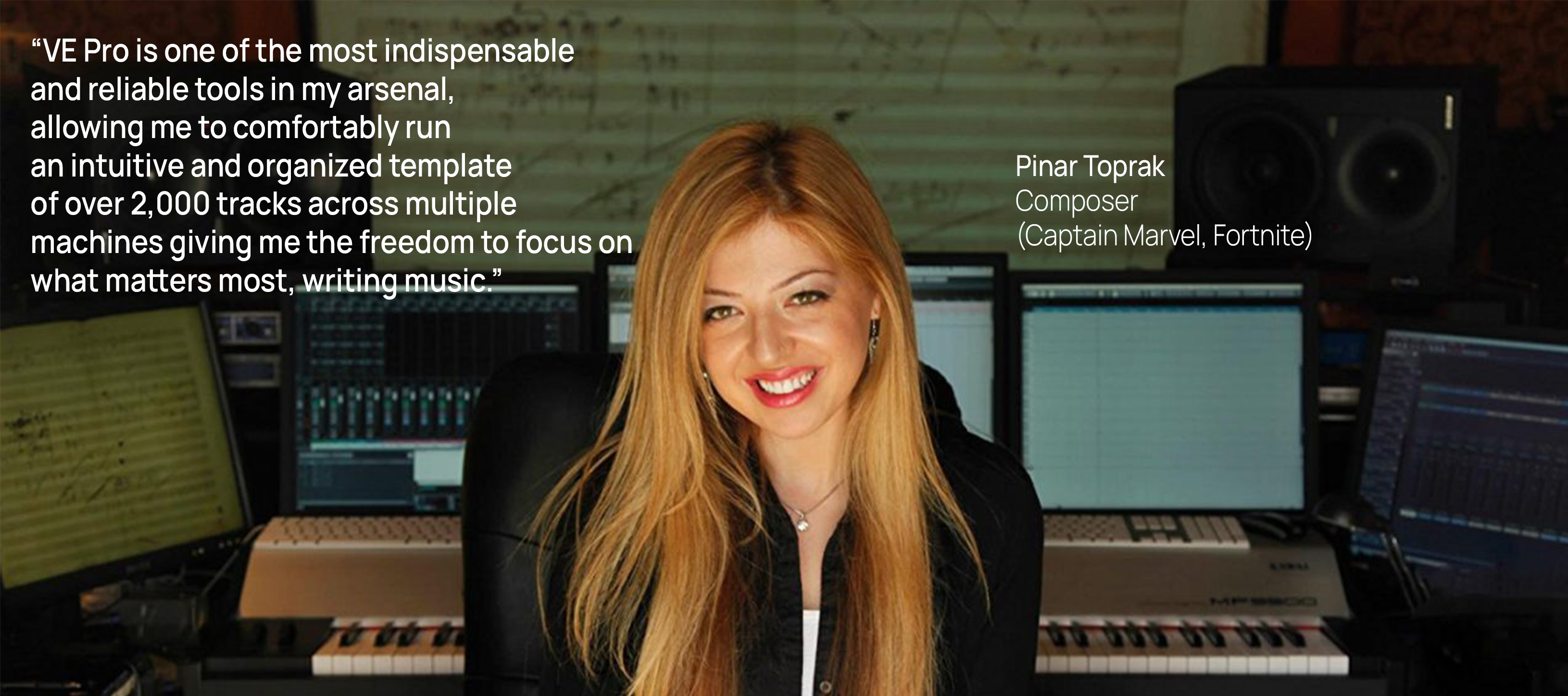 Pinar Toprak, composer for Captain Marvel and Fortnite, smiling in her music studio with keyboards, multiple computer monitors showing audio software, and studio speakers.