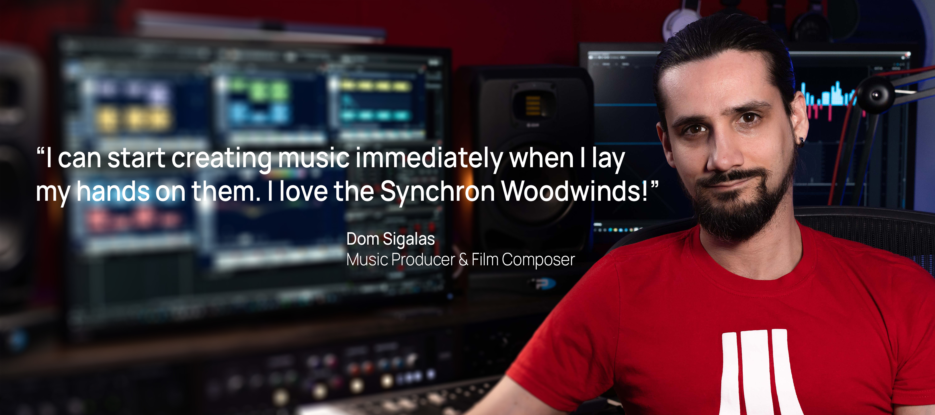 Dom Sigalas, Music Producer and Film Composer, in his studio, wearing a red shirt, with computer monitors displaying music production software in the background.